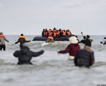 Migrants wave to a smuggler's boat in an attempt to cross the English Channel, on the beach of Gravelines, near Dunkirk, northern France on April 26, 2024. - Five migrants, including a seven-year-old girl, died on April 23, 2024 trying to cross the Channel from France to Britain, local authorities said, just hours after Britain passed a controversial bill to deport asylum seekers to Rwanda. (Photo by Sameer Al-DOUMY / AFP)